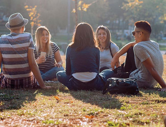 Skupina mladých lidí v městském parku sedí v kroužku na trávě.